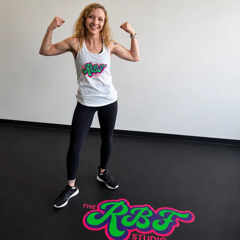 Kayla, Founder of Ridiculous Fitness, flexing in the studio over the RBF floor logo